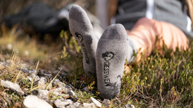 A person is lying in a meadow; in the foreground, their feet can be seen wearing grey socks with a logo.