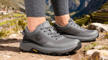 A close-up of a woman’s feet wearing grey Giesswein outdoor shoes with a waterproof membrane; in the background, a rocky mountain landscape with terraced fields in Peru.