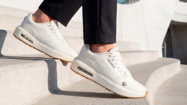 A close-up of white Giesswein trainers with visible air-cushioned soles and black trousers, as the wearer climbs a light-coloured stone staircase.