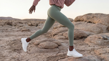 A woman running across rocky ground, visible from the waist down. She is wearing mint-green leggings; the top of a dusky pink sleeve can be seen at the top of the picture, and she is wearing white Giesswein trainers on her feet.