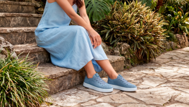 A close-up of feet in light blue knitted trainers with white soles on stone steps, accompanied by a light blue linen dress and a cobbled path in the foreground.