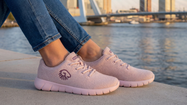 A close-up of two feet in pink Wooltastic trainers by Giesswein, standing on a wall with a river and a bridge in the background.