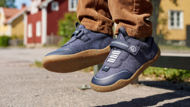 A close-up of a child’s dangling feet in brown corduroy trousers. The child is wearing dark blue merino wool children’s shoes.