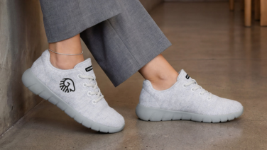 A close-up of a woman’s legs in grey trousers and cream-coloured merino trainers by Giesswein on a concrete floor.