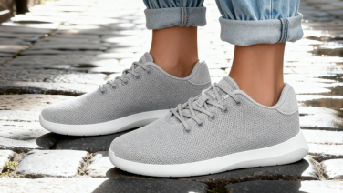 Close-up of a light grey Giesswein merino sneaker with a white sole on cobblestones, worn with rolled-up jeans.