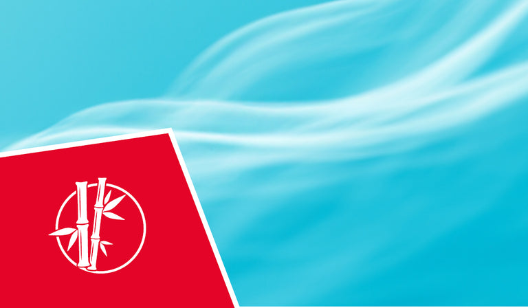 A bright blue sky with soft white wispy clouds in the background. In the lower left corner is a red square icon featuring a white circular logo with bamboo stalks and leaves inside it, representing natural and sustainable materials.