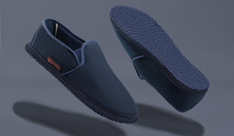A pair of navy blue Giesswein slip-on shoes with textured canvas uppers and rubber soles, shown from side and bottom views against a gray background.