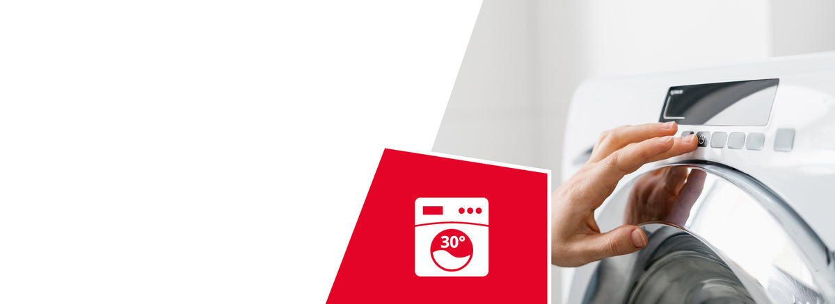 A person's hand adjusting the control dial of a white washing machine. A red icon shows a washing machine symbol with "30°" indicating machine washable at 30 degrees Celsius.