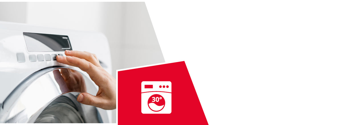 A person's hand reaches out to press a button on the control panel of a modern, white washing machine. In the foreground, a red triangular overlay with a white icon featuring a washing machine and "30°" inside a drum is visible in the bottom right corner.