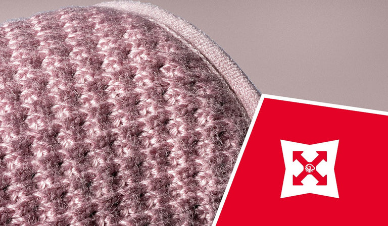 Close-up of pink and gray knitted wool fabric showing detailed texture and stitching. A red icon displays a white shield with arrows, indicating durability or strength properties.