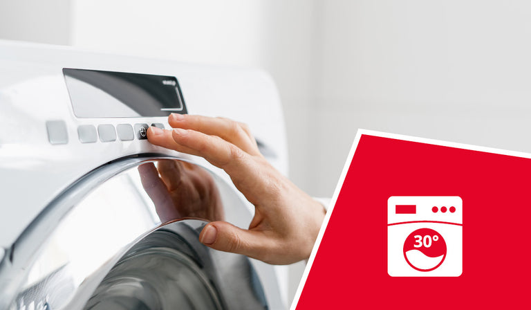 A person's hand reaches out to press a button on the control panel of a modern, white washing machine. In the foreground, a red triangular overlay with a white icon featuring a washing machine and "30°" inside a drum is visible in the bottom right corner.