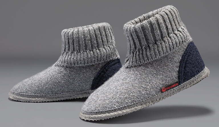 A pair of gray wool slipper boots with ribbed knit ankle cuffs and navy blue heel accents, featuring the Giesswein brand label, against a neutral gray background.