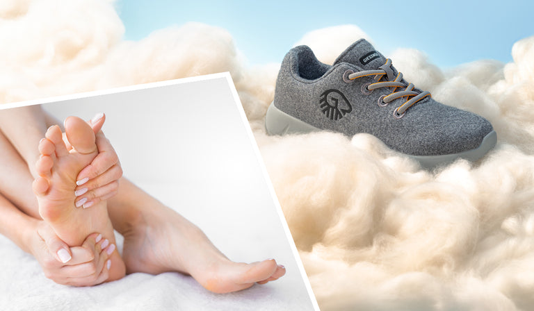 A soft grey orthopedic shoe with beige laces rests on fluffy white wool, suggesting extreme comfort. The shoe features a black embroidered logo and a label that reads “GIESSWEIN.” In the bottom left, there's an inset image of a person gently massaging their bare foot, emphasizing foot care and relief. The background is light and airy, enhancing the feeling of softness and comfort.