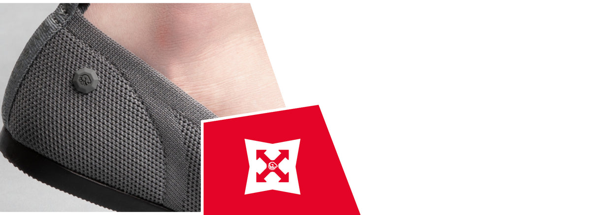 Close-up of a person's foot wearing a gray knitted slip-on shoe with textured upper and a small logo button. A red icon shows a white shield with arrows, indicating durability or strength properties.