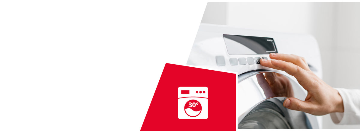 A person's hand adjusting the control dial of a white washing machine. A red icon shows a washing machine symbol with "30°" indicating machine washable at 30 degrees Celsius.