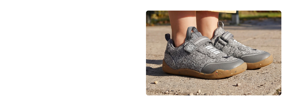 Close-up of grey Giesswein children’s trainers with a merino upper, Velcro fastening and honey-coloured sole on a sandy path.