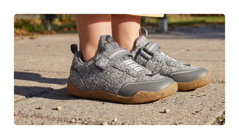 Close-up of grey Giesswein children’s trainers with a merino upper, Velcro fastening and honey-coloured sole on a sandy path.
